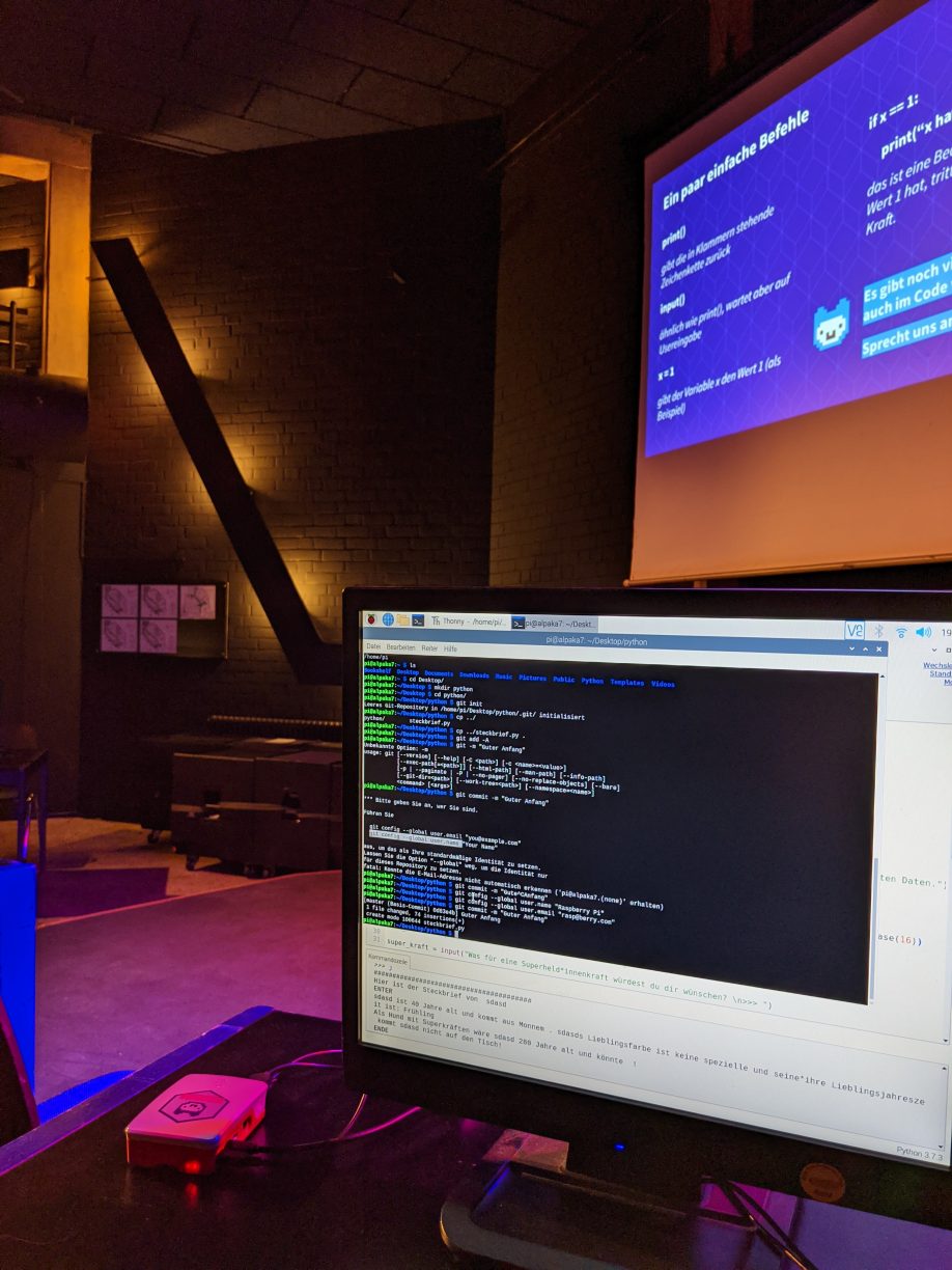 Ein Computermonitor mit Programmcode steht in einem bunt ausgeleuchtetem Raum.