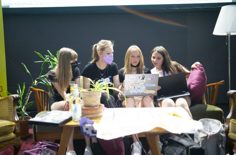 3 Teilnehmerinnen sitzen auf einem Sofa zusammen mit einer Mentorin und schauen alle auf einen Laptop mit Jugend Hackt Stickern.