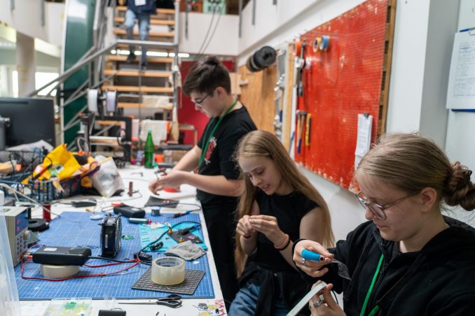 Jugendliche löten und basteln an einer Löt-Arbeitsfläche an einem LED-Streifen.